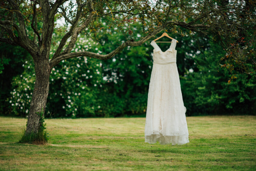 A wedding dress hangs from a tree on the morning of a wedding.