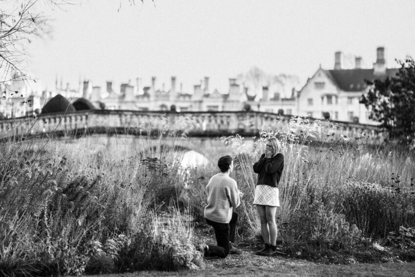 A man proposes to his girlfriend on one knee in the beautiful gardens of Clare College. Clare Bridge can be seen in the background.