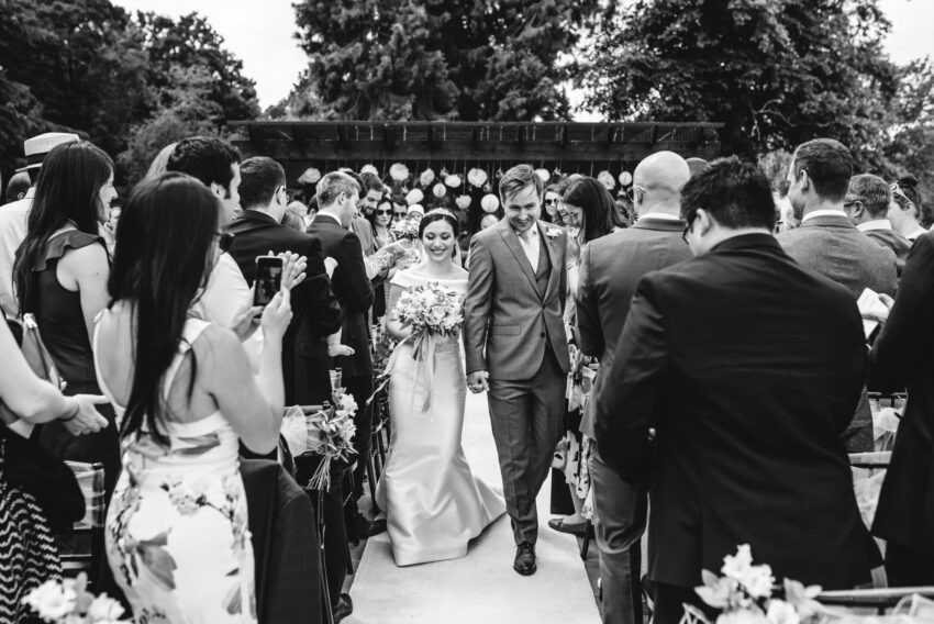 A bride and groom leave their outdoors wedding ceremony hand in hand.
