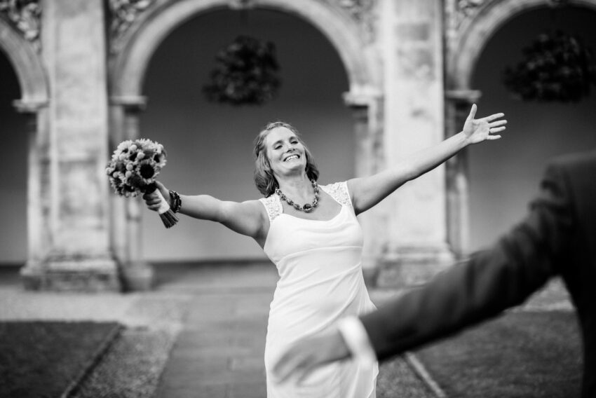 Bride celebrating with arms outstretched in the cloisters at Magdalene College, Cambridge
