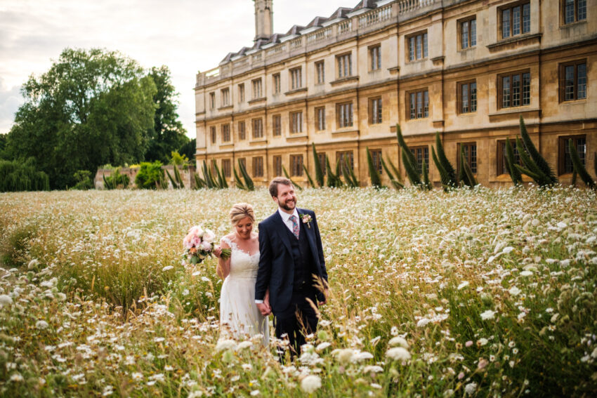 Bride and groom walking through wildflowers in the grounds of King’s College, Cambridge