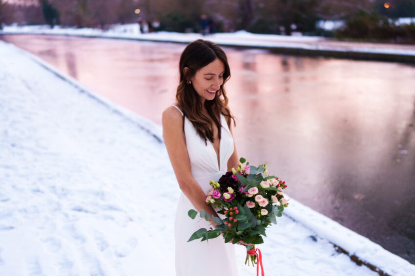 Bride standing by the River Cam at winter sunset, holding her bouquet