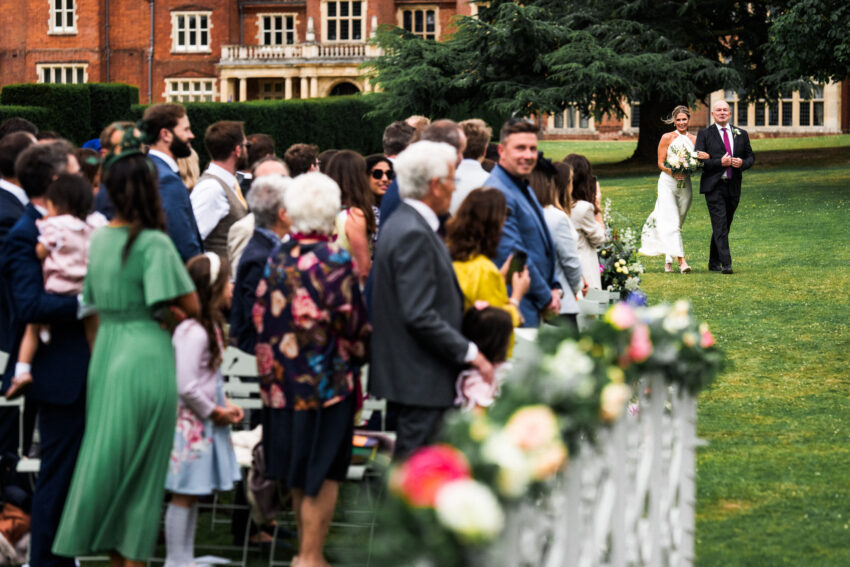 Wedding ceremony taking place outdoors at Longstowe Hall, with guests watching from the lawn