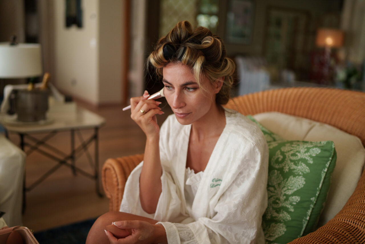 Bride having her makeup finished in a robe during calm wedding morning preparations