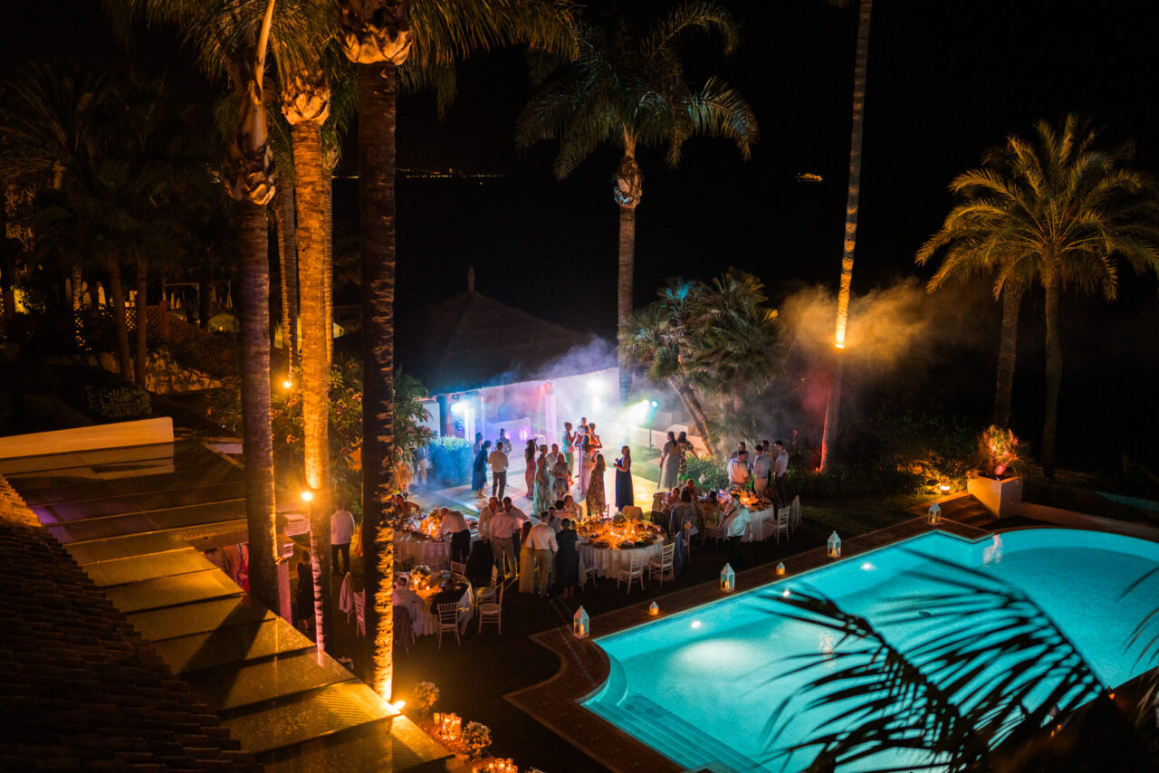 Night-time aerial view of a poolside wedding reception with lights and dancing in southern Spain