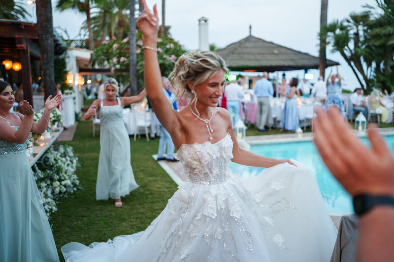 Bride dancing by the pool during an evening wedding celebration in Marbella