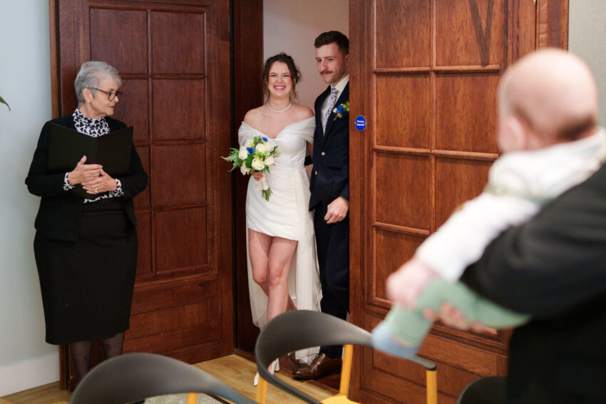 Bride and groom entering the ceremony room at Camden Town Hall, greeted by the registrar and guests.
