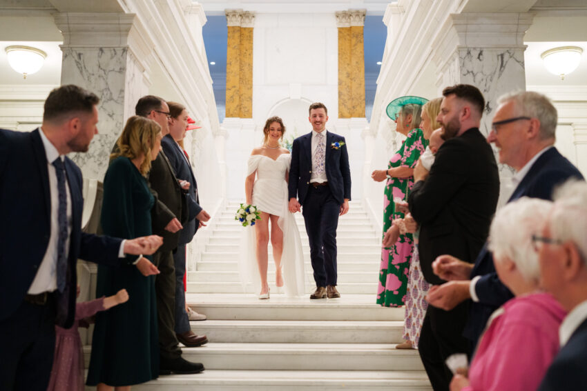 Bride and groom walking down the staircase as guests throw confetti.