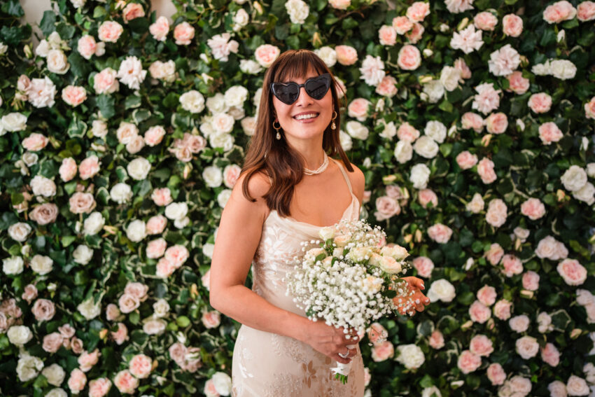 Bride portrait in sunglasses in front of a flower wall at Chelsea Old Town Hall.