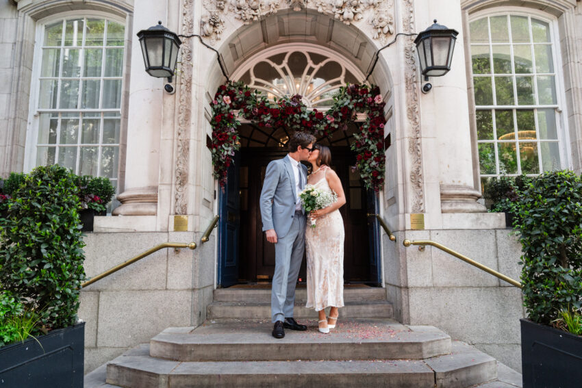 Bride and groom kissing outside Chelsea Old Town Hall under the floral arch.