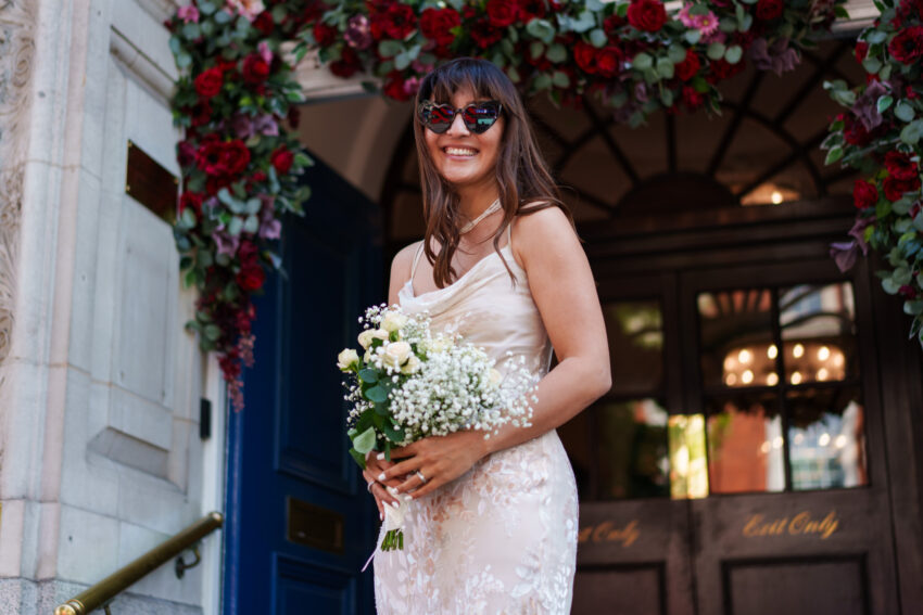 Bride in sunglasses holding her bouquet outside Chelsea Old Town Hall