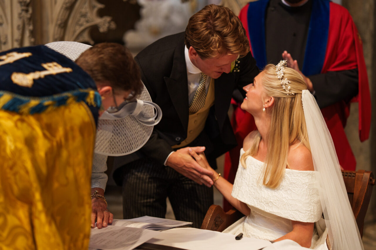 Bride and groom signing the register during a church ceremony, soft interior light and close framing drawing attention to hands and gesture, photographed by an Ely wedding photographer.