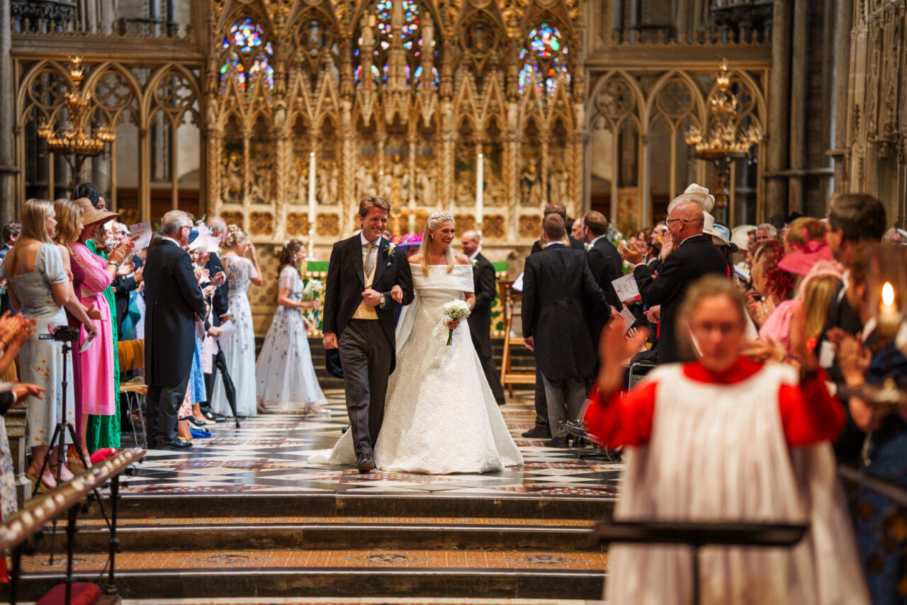 The couple walking back down the aisle together, guests standing on either side, patterned stone floor and warm candlelight leading the eye forward.