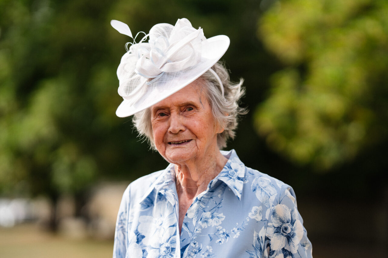 Portrait of a wedding guest wearing a light blue outfit and hat, shallow depth of field separating the subject from the soft green background.