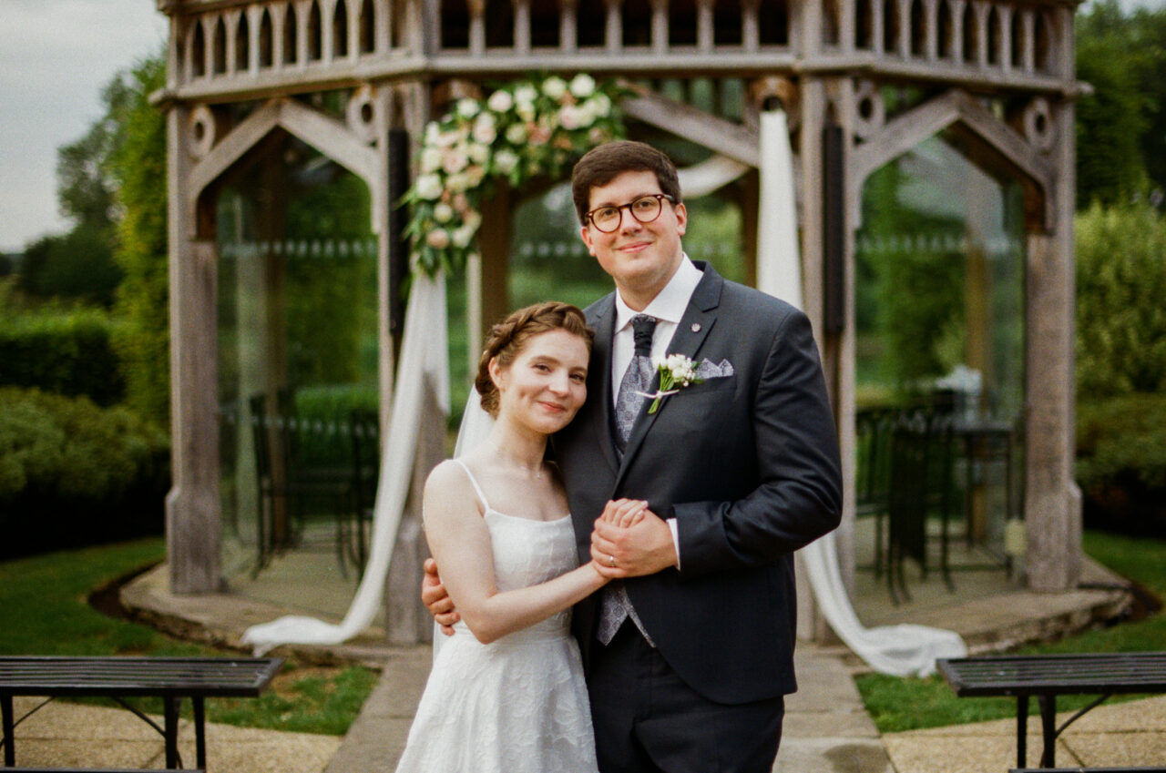Bride and groom standing together beneath the pavilion, shallow depth of field and symmetrical framing drawing focus to the couple.