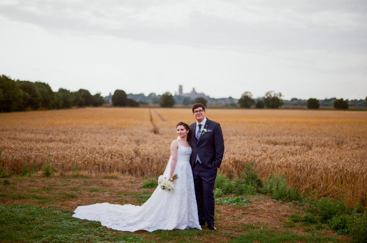 Portrait of the couple standing at the edge of open fields, muted skies and natural tones keeping the setting understated.