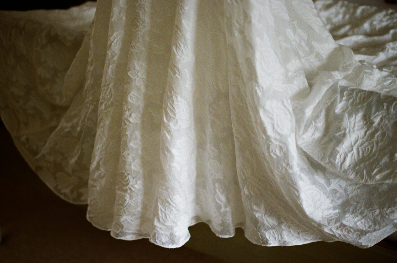 Close detail of the wedding dress fabric, natural window light revealing texture and movement in the material.