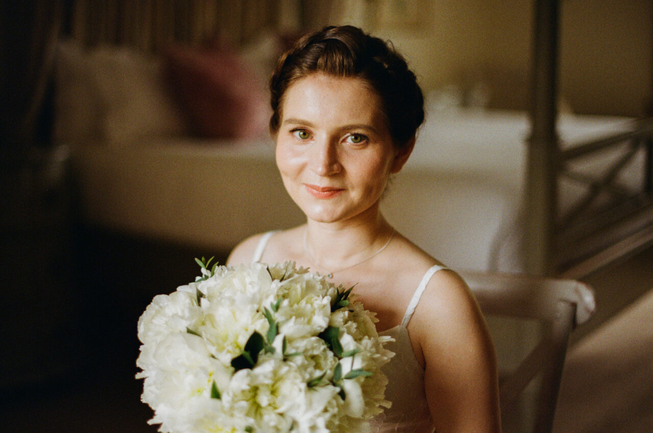 Close portrait of the bride holding her bouquet indoors, soft directional light and shallow focus isolating the subject.