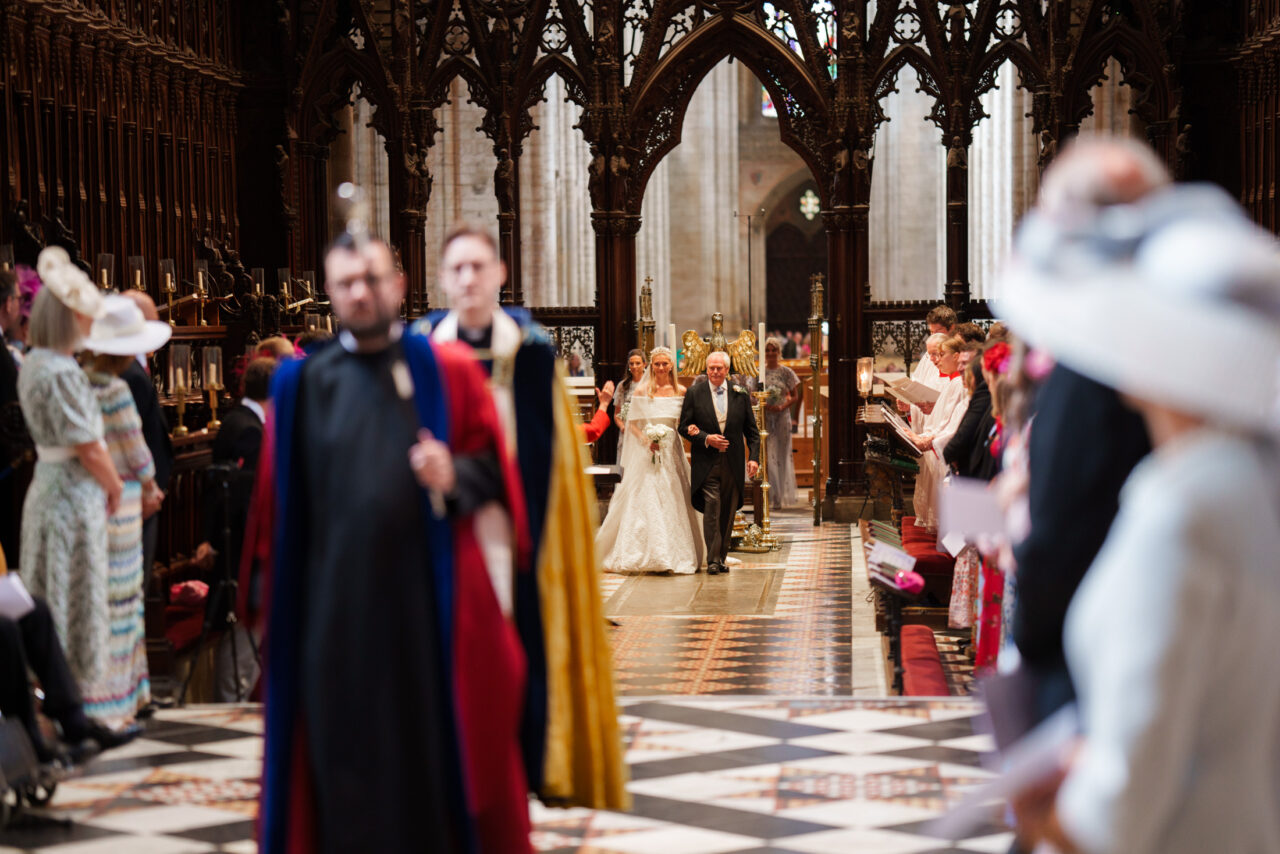 Processional moment framed through seated guests, movement and architecture shaping the composition inside the church.