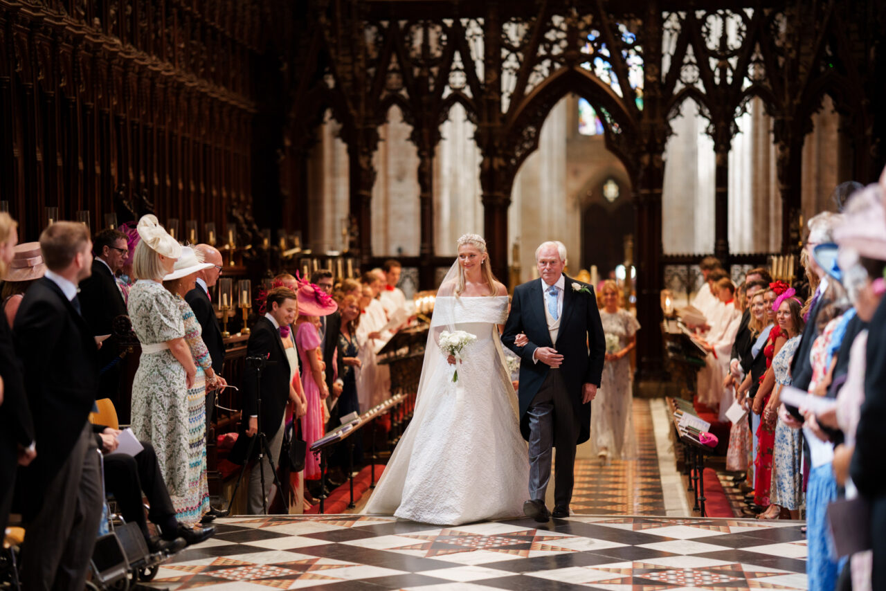 Processional moment framed through seated guests, movement and architecture shaping the composition inside the church.
