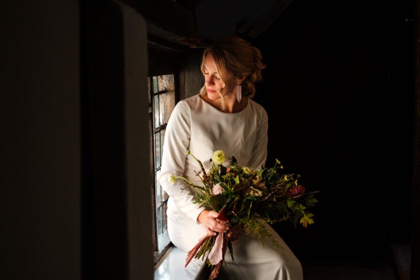 Bride holding a bouquet indoors, soft light and reflective mood.