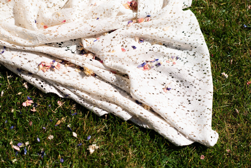 Wedding dress hem resting on grass, confetti scattered across fabric.