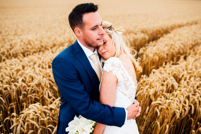 Couple holding each other in a wheat field, warm and intimate atmosphere.