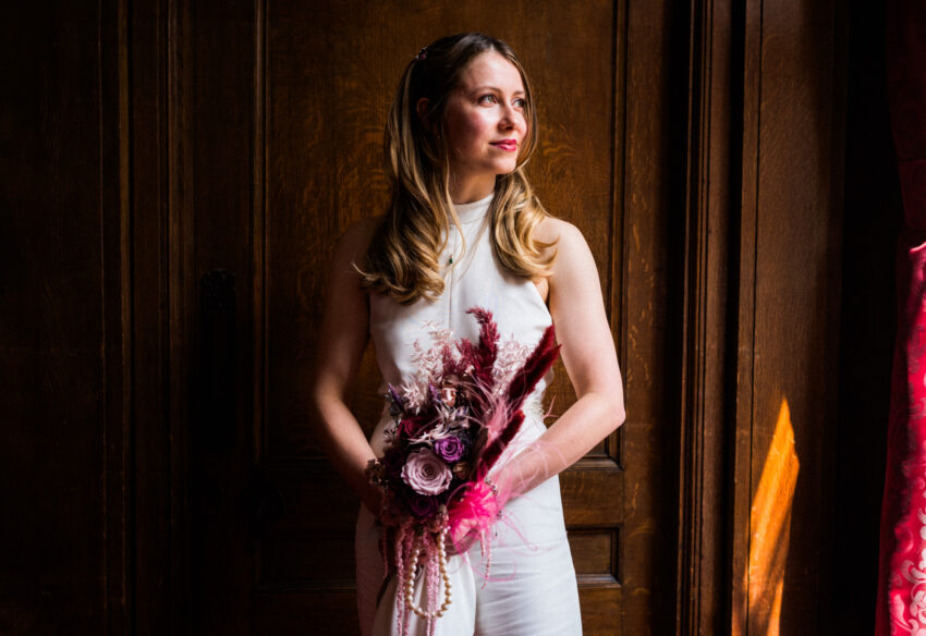 Bride holding a bouquet by a doorway, natural light and thoughtful mood.