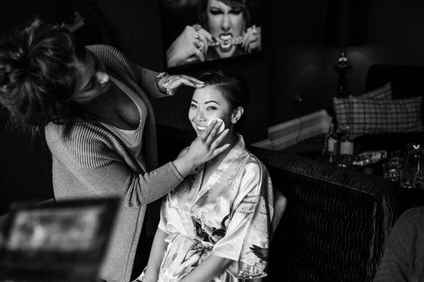 Bride having makeup applied, candid black and white morning preparation.