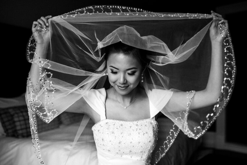 Bride smiling beneath her veil, soft light and gentle expression.