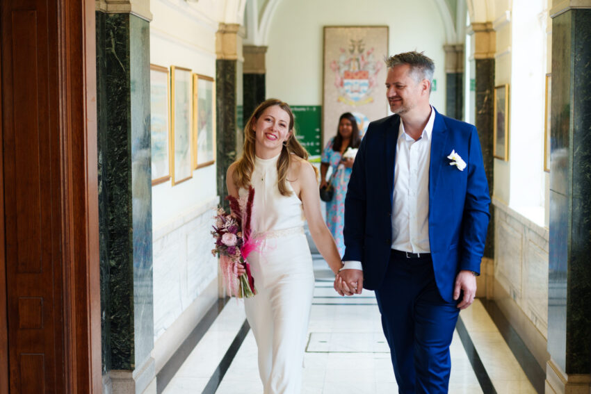 Bride and groom walking together through the corridors of Islington Town Hall after their wedding ceremony.