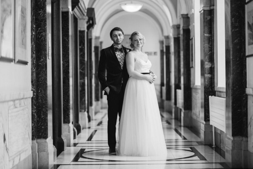 Bride and groom standing together in the bright marble corridors at Islington Town Hall during their wedding, photographed in black and white.