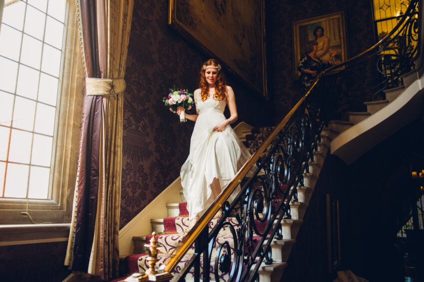 Bride walking down a grand staircase in a historic interior.