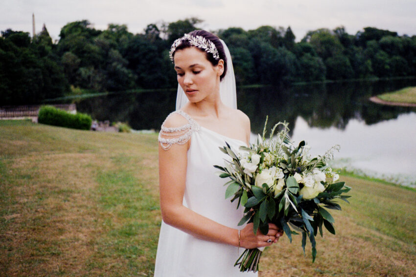 Bride holding a bouquet beside a lake.