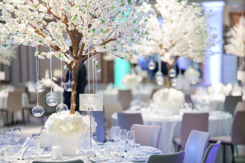 Wedding reception table set with white tablecloths, glassware, candles, and tall floral centrepieces arranged beneath soft lighting at Kimpton Fitzroy London.