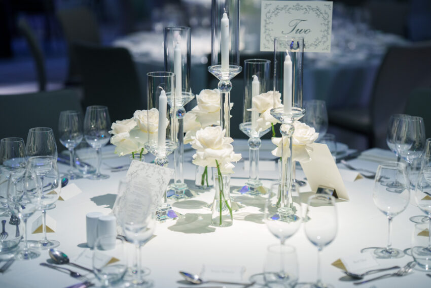Close-up of elegant wedding table details with white flowers, candles in glass holders, menus, and neatly arranged cutlery.