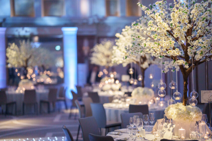 Wide view of the evening wedding reception room at Kimpton Fitzroy London, with softly lit tables, floral arrangements, and blue uplighting around the space.