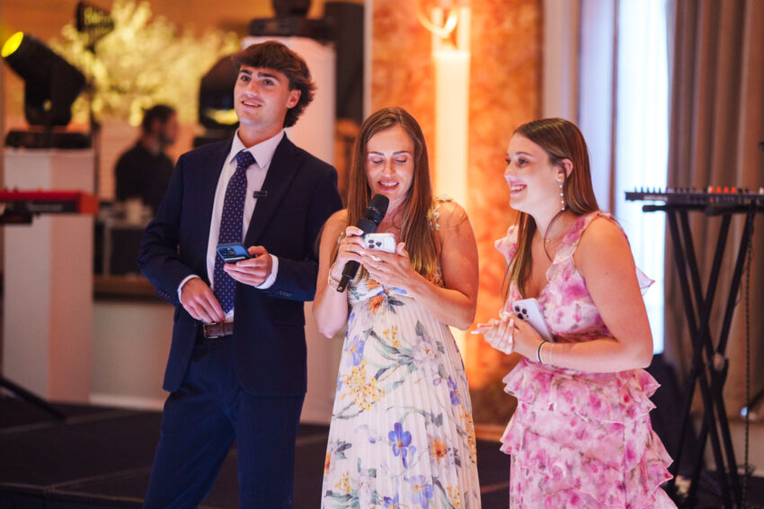 Wedding guests standing together at the reception holding microphones and notes while delivering speeches at Kimpton Fitzroy London.