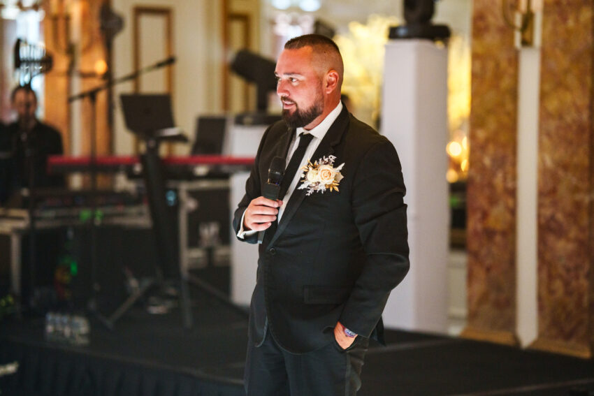 Wedding guest delivering a speech while holding a drink, standing in front of musical equipment during the reception at Kimpton Fitzroy.