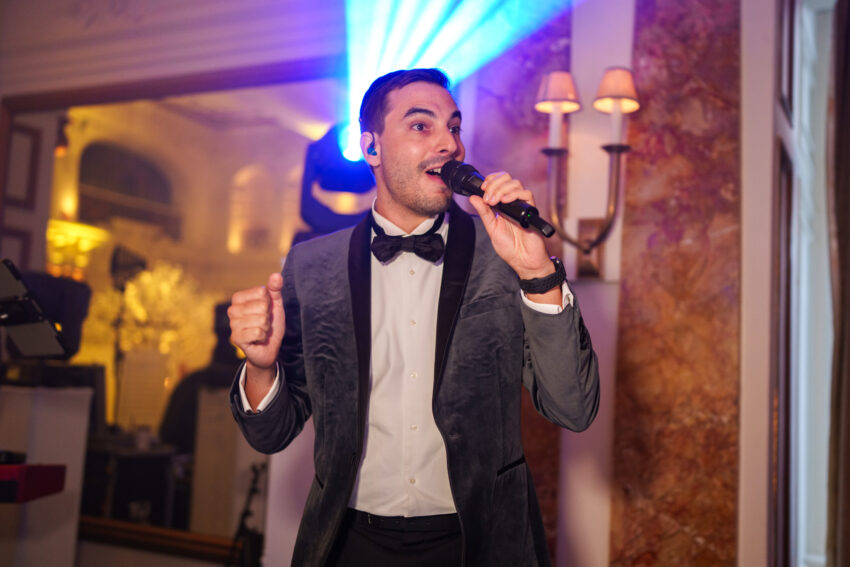 Wedding singer performing into a microphone on stage, illuminated by coloured lights during the evening reception at Kimpton Fitzroy London.