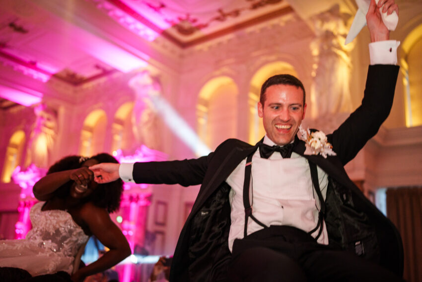 Evening celebration scene with the groom dancing under pink and purple reception lighting inside Kimpton Fitzroy London.
