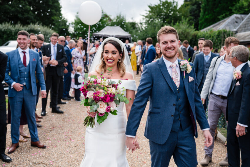 Couple smiling as they walk hand in hand through their guests after the ceremony, confetti scattered on the ground.