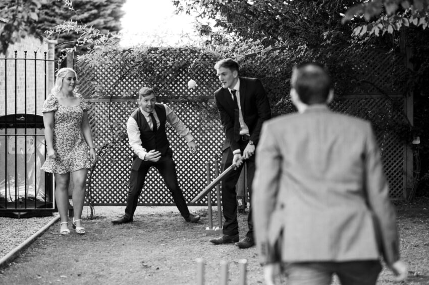 Guests playing garden games during the reception, captured in black and white with relaxed movement and laughter.