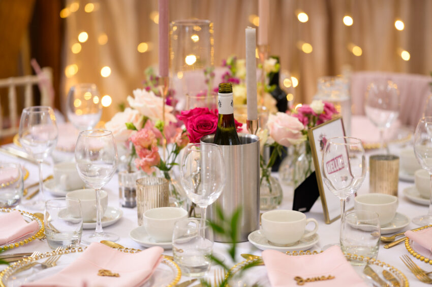 Wedding table details with candles, glassware, floral arrangements and soft lighting inside the reception space.
