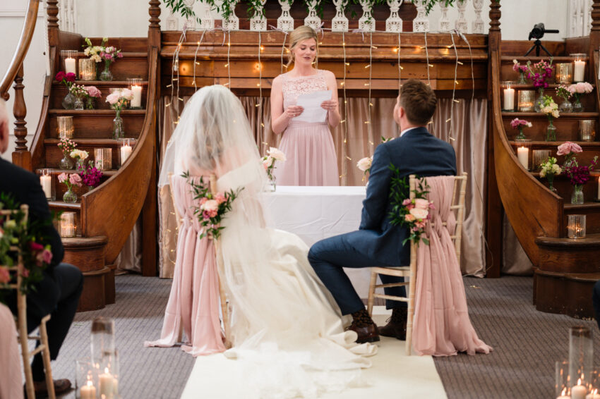 Bride and groom facing the registrar during the ceremony at Kings Chapel, framed by wooden architecture and flowers.