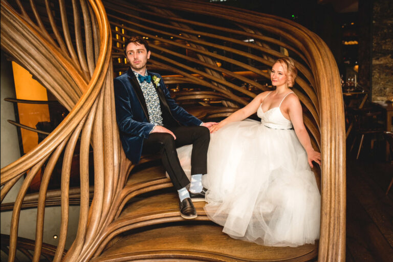 Bride and groom seated inside a stylish London venue with sculptural wooden interior