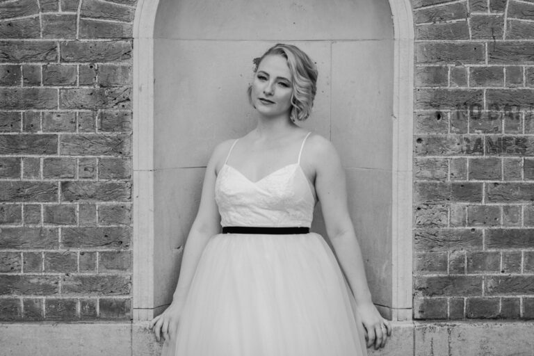 Black and white bridal portrait by a brick archway, elegant wedding photography