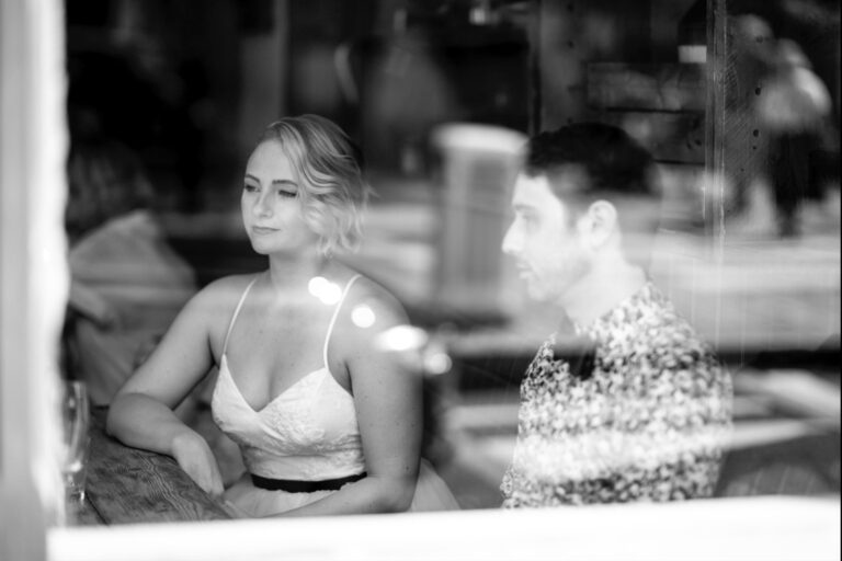 Black and white photo of bride and groom seen through a window, candid London couple photoshoot moment