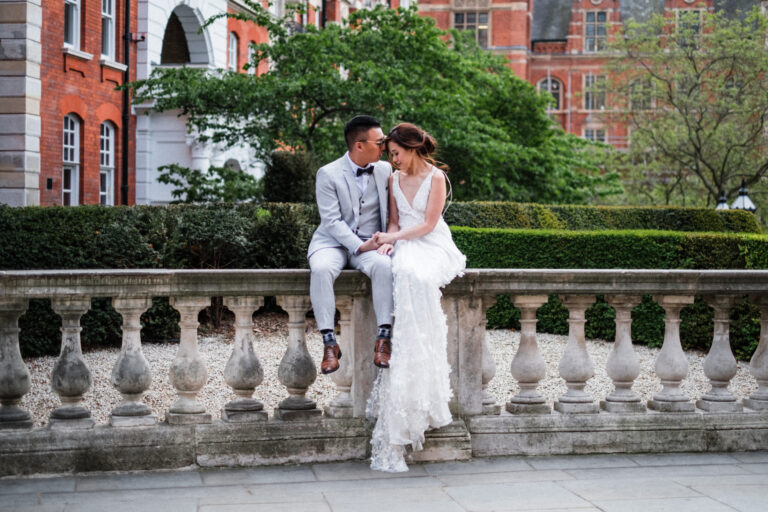Bride and groom sitting on a stone balustrade in a garden courtyard in Kensington.