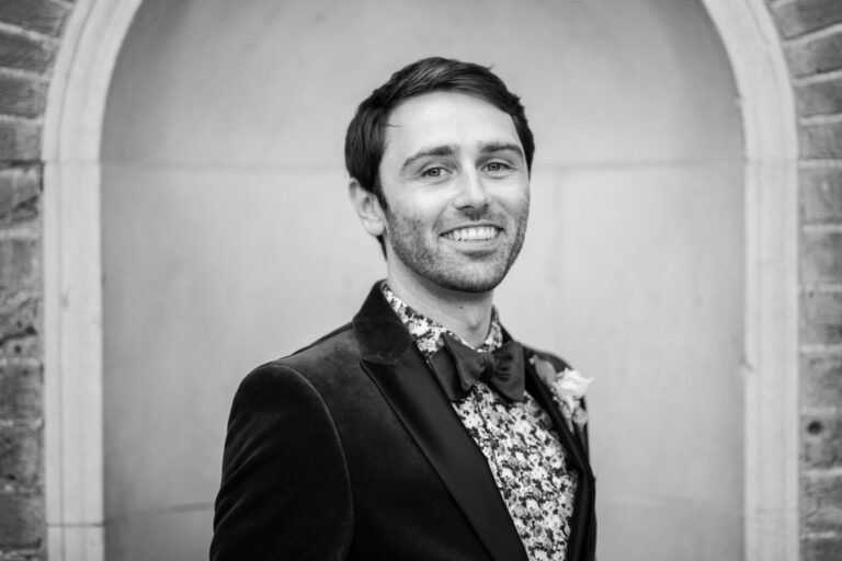 Black and white groom portrait by a brick archway, classic wedding photography